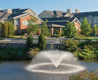 Exterior view of Brooksby Village with brick buildings, trees, and a fountain pond.