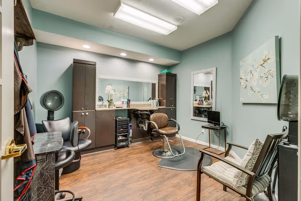 Salon room with styling chairs, mirrors, cabinetry, and a hooded hair dryer in a mint-green painted interior.