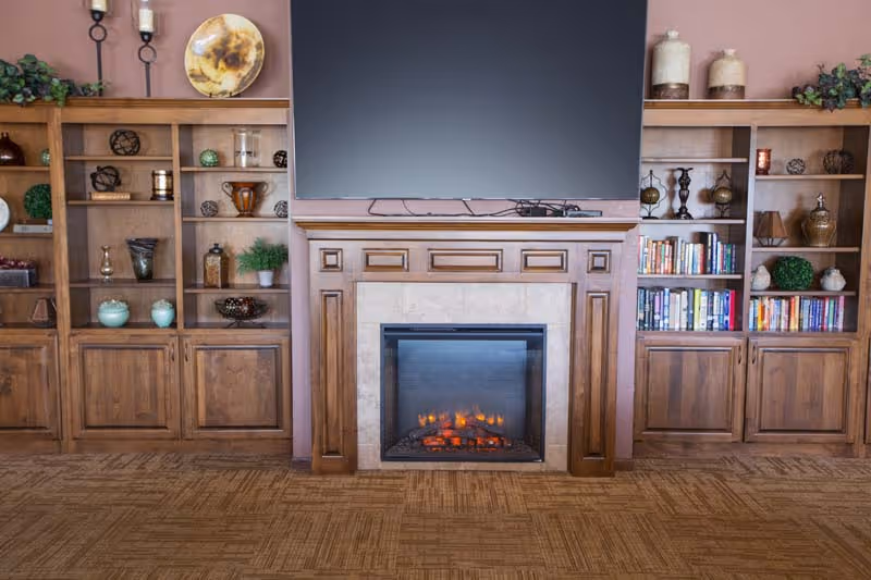 A wood-framed fireplace with a flat-screen TV above, flanked by built-in wooden bookshelves holding books and decorative items.