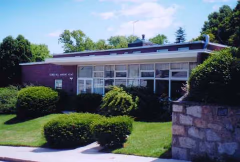 A single-story building with large windows and neatly trimmed shrubs on a green lawn.