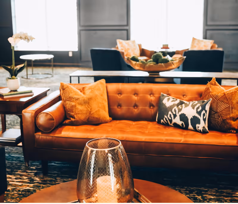 A stylish lounge area with an orange tufted leather sofa, patterned pillows, and a coffee table topped with a glass candle holder.