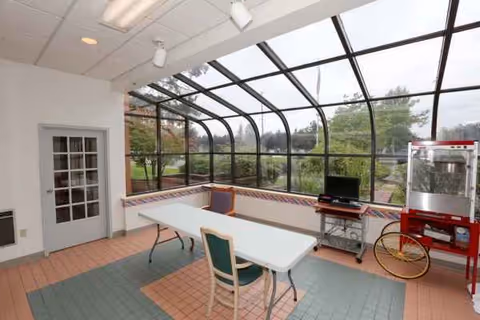 Enclosed sunroom with curved glass walls, folding table, chairs, and a red popcorn machine.