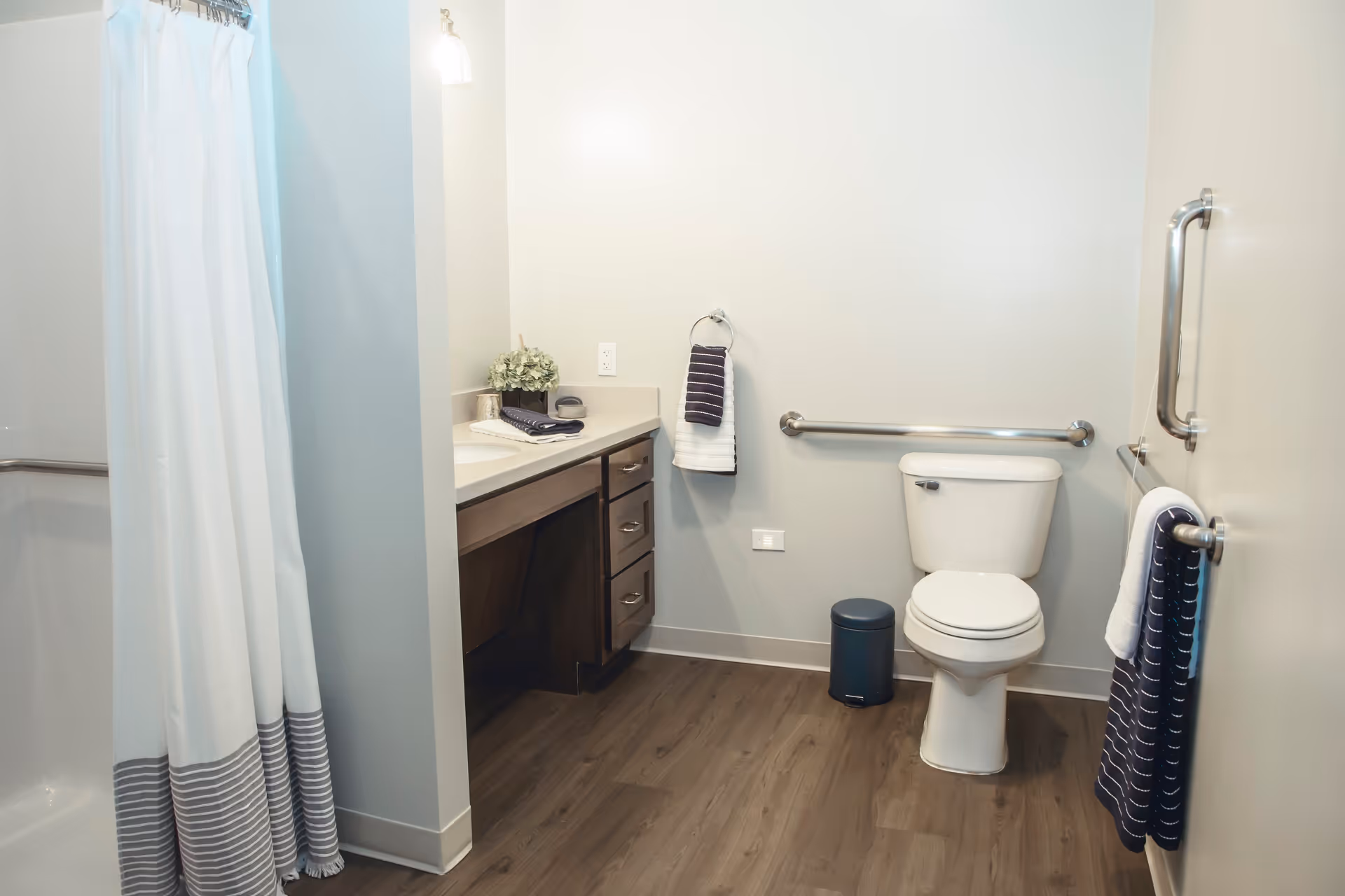 Accessible bathroom with a toilet, grab bars, vanity with countertop and drawers, and a shower with a striped curtain.