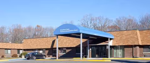 Exterior of Autumn Lake Healthcare entrance with a blue canopy and parked car.