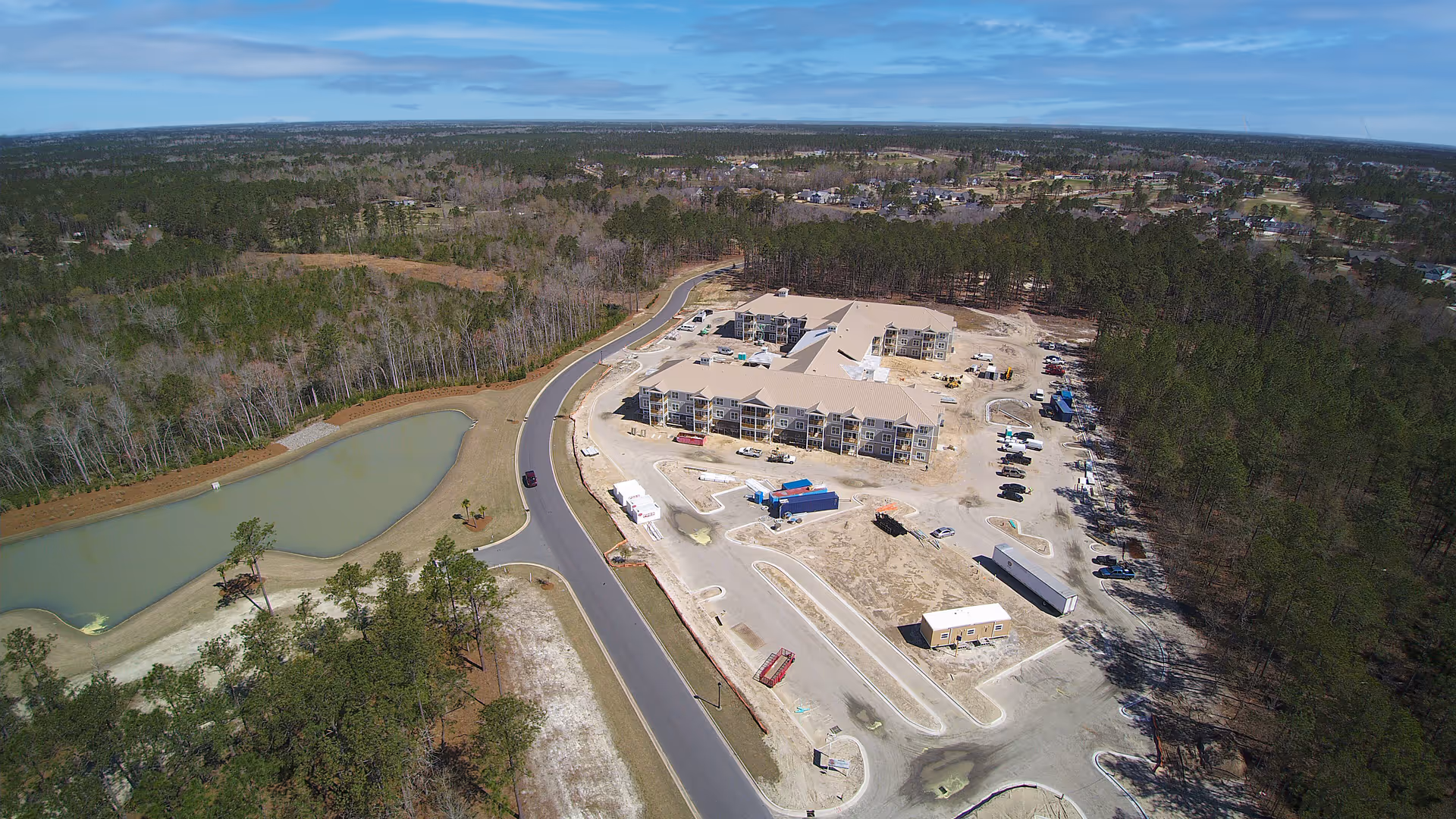 Aerial view of the Arbor Landing at Compass Pointe complex under construction bordered by trees, a road, and a pond.