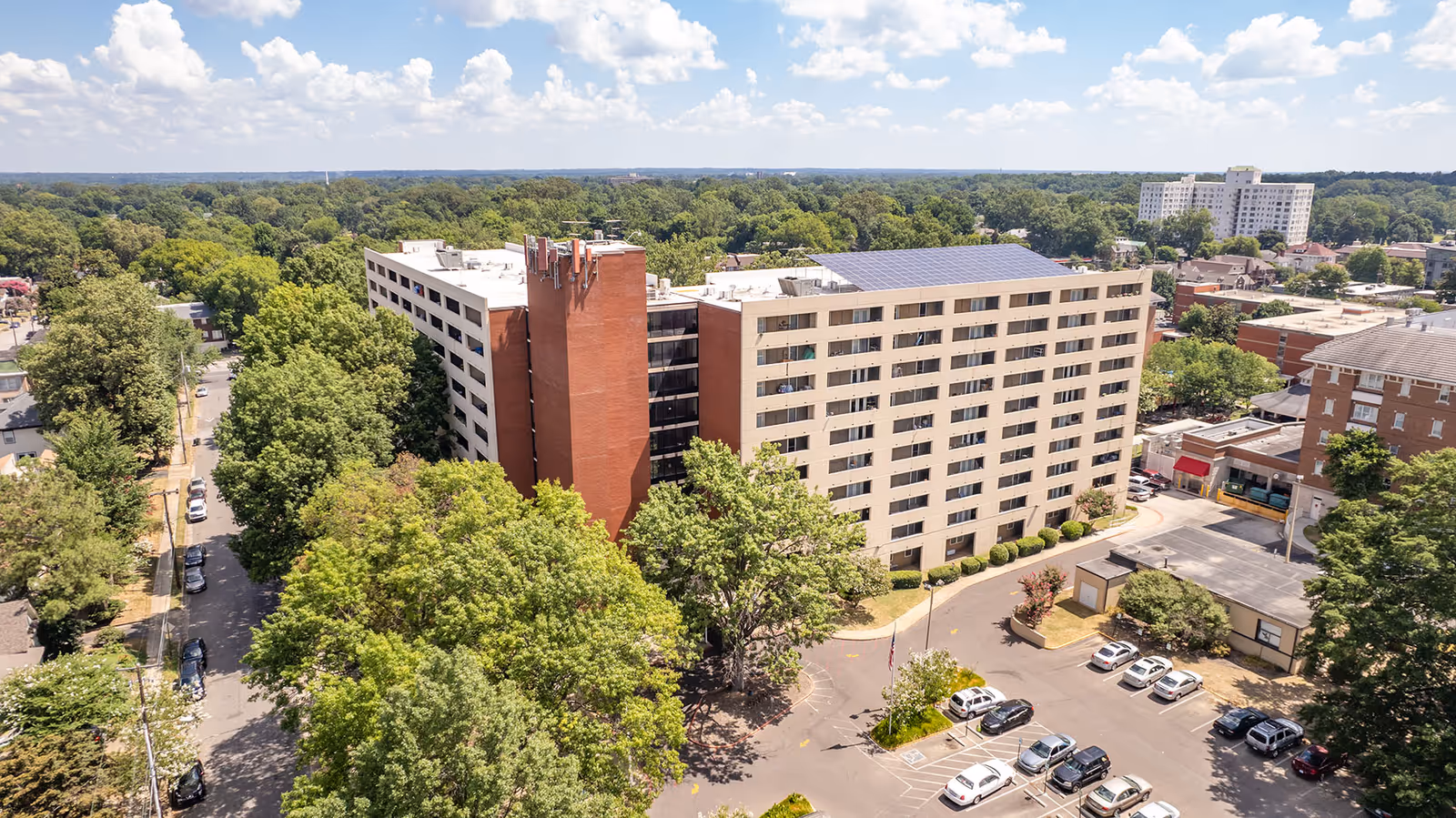 Aerial view of St. Peter Manor, a beige, multi-story senior living building surrounded by trees with a parking lot nearby.
