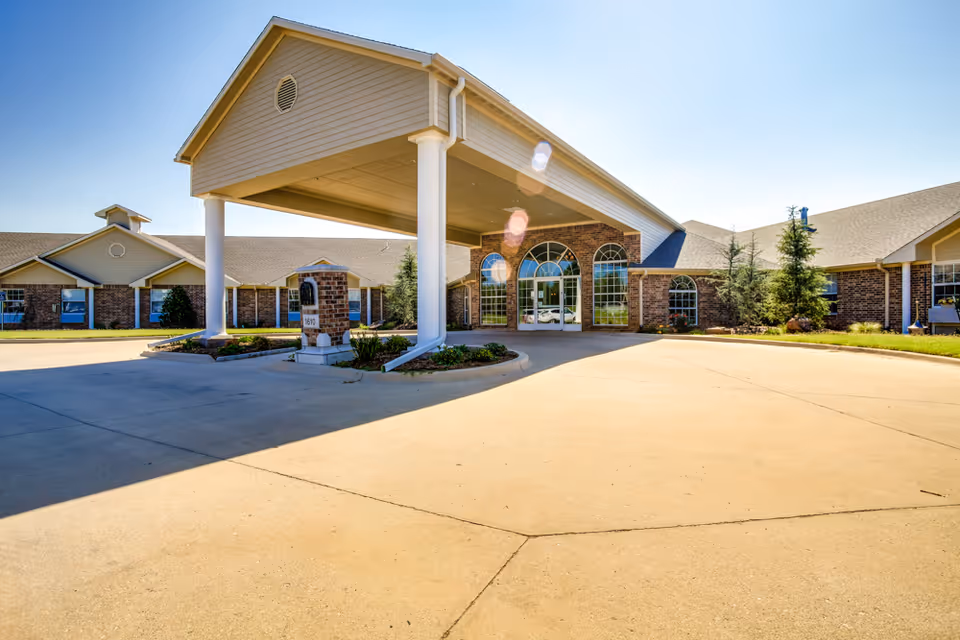 Front entrance of The Regency Skilled Nursing & Therapy showing a covered porte-cochere and driveway leading to glass double doors of a brick building.