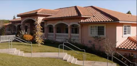 Single-story pink stucco senior living facility with tiled roof and arched entrance.