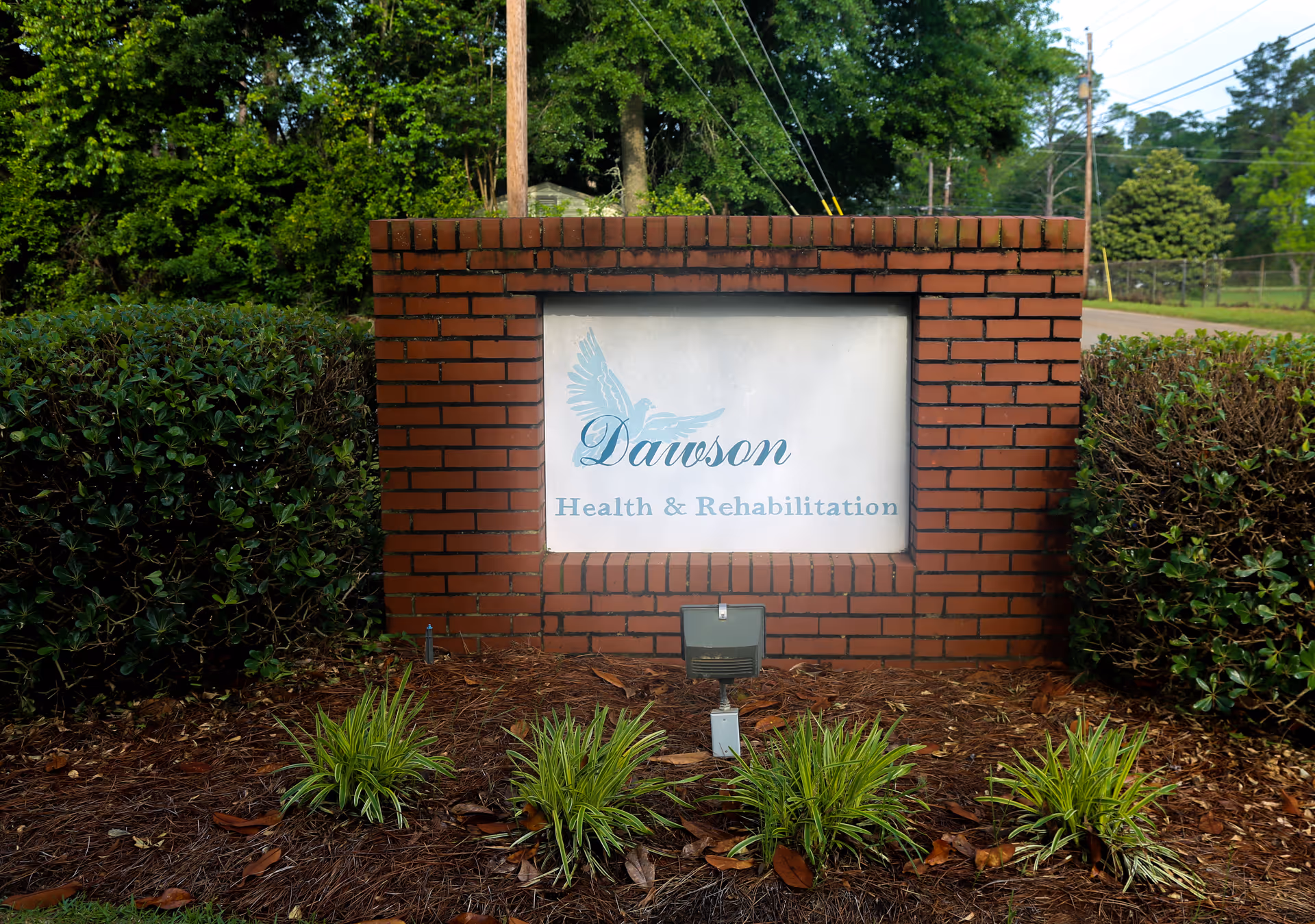 Brick entrance sign reading "Dawson Health & Rehabilitation" framed by shrubs and landscaping.