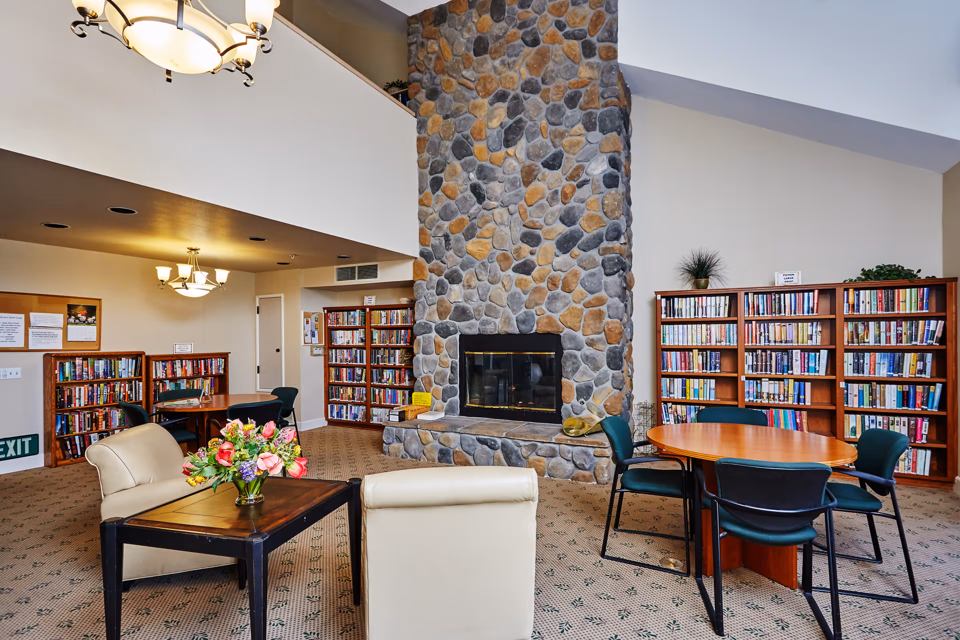 Cozy communal library/reading room with a large stone fireplace, bookshelves, tables and seating.