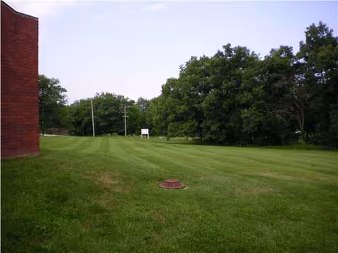 Open grassy lawn beside a brick building with distant trees.