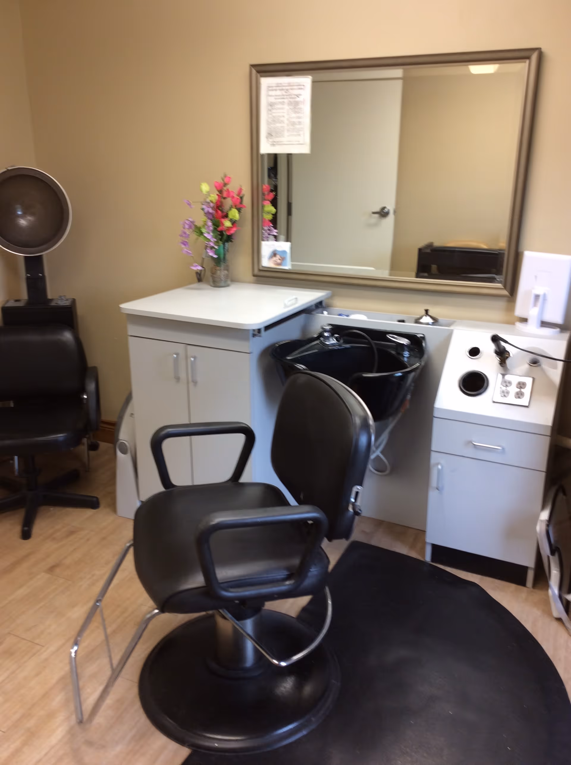 A salon styling station with a black salon chair, shampoo sink, mirror, and cabinets.