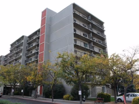 Exterior view of a tall multi-story care home building with trees and a street in front.