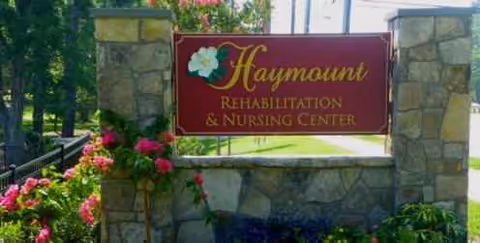 Outdoor entrance sign reads Haymount Rehabilitation & Nursing Center beside stone pillars and flowers.