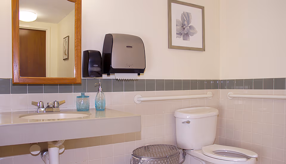 Accessible restroom with a sink and mirror on the left, paper towel and soap dispensers, grab bars, and a toilet on the right.