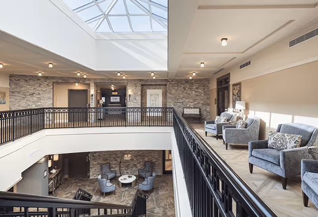 Bright two-story atrium lounge with a skylight, railings, and upholstered seating on both levels.