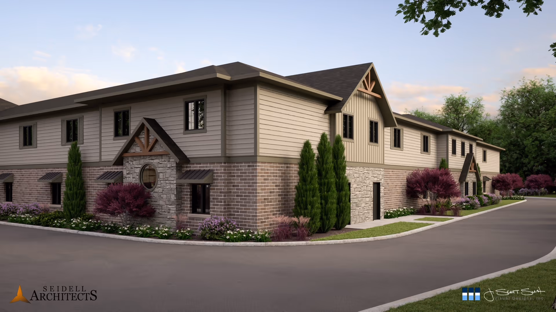Exterior view of a two-story senior living facility building with a combination of brick, stone, and siding on the facade. The building is surrounded by landscaped greenery including bushes, trees, and flowers, with a paved driveway curving around it under a partly cloudy sky.