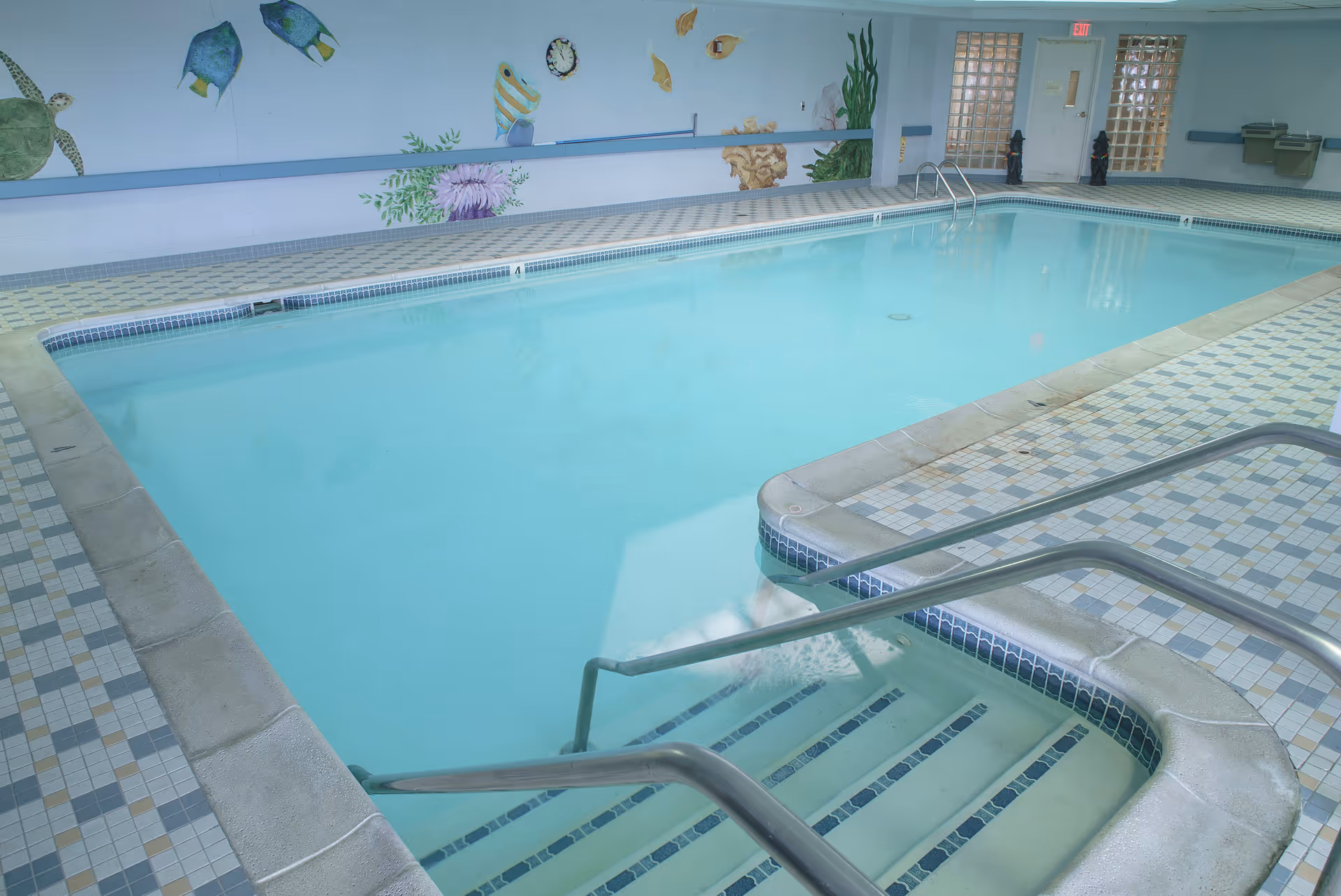 Indoor swimming pool with tiled deck, steps and handrails, and a fish-and-sealife mural on the far wall.