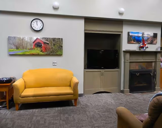 Yellow sofa in a cozy senior living lounge with television, fireplace, and wall art.