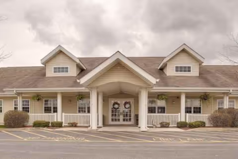 Senior living facility exterior with a covered front entrance, wreaths, and a parking lot.