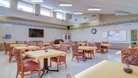 An empty dining room at SKLD Whitehall, with multiple tables and red-upholstered chairs.
