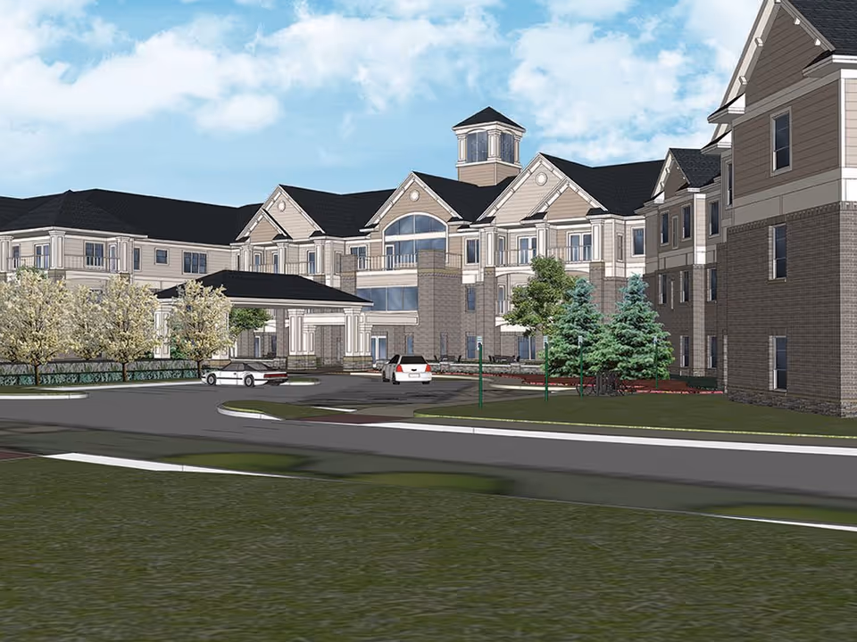 Architectural rendering of a large senior living facility building with multiple floors, a covered entrance, several windows, and a tower-like structure on the roof. The scene includes a driveway with two cars, landscaped greenery, trees, and a partly cloudy sky.