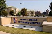 Stone entrance sign reading "Gino J. Merli Veterans Center" with the facility building and landscaping behind it.