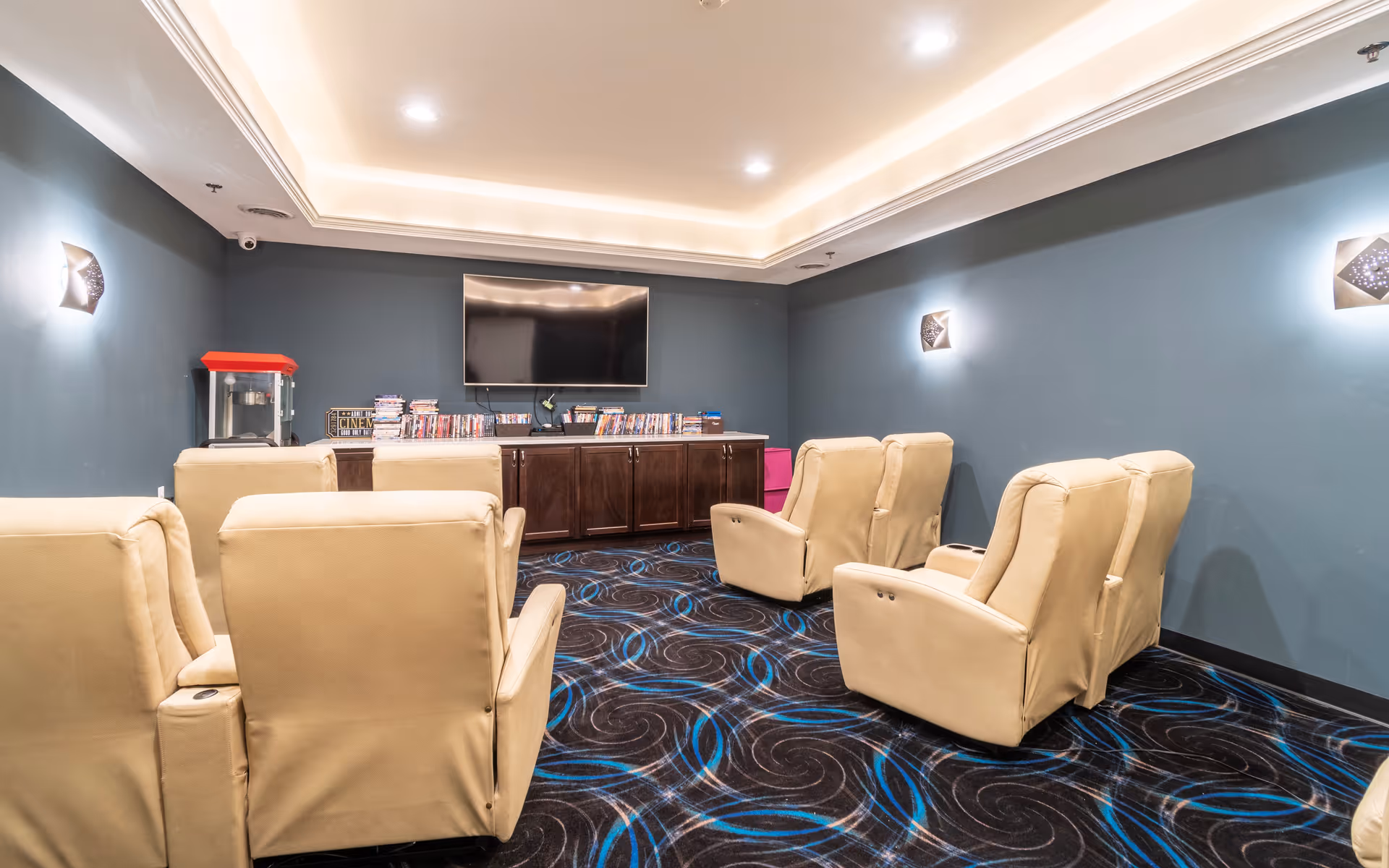 A cozy media room with beige recliner chairs facing a wall-mounted TV, a popcorn machine, and shelves of DVDs.