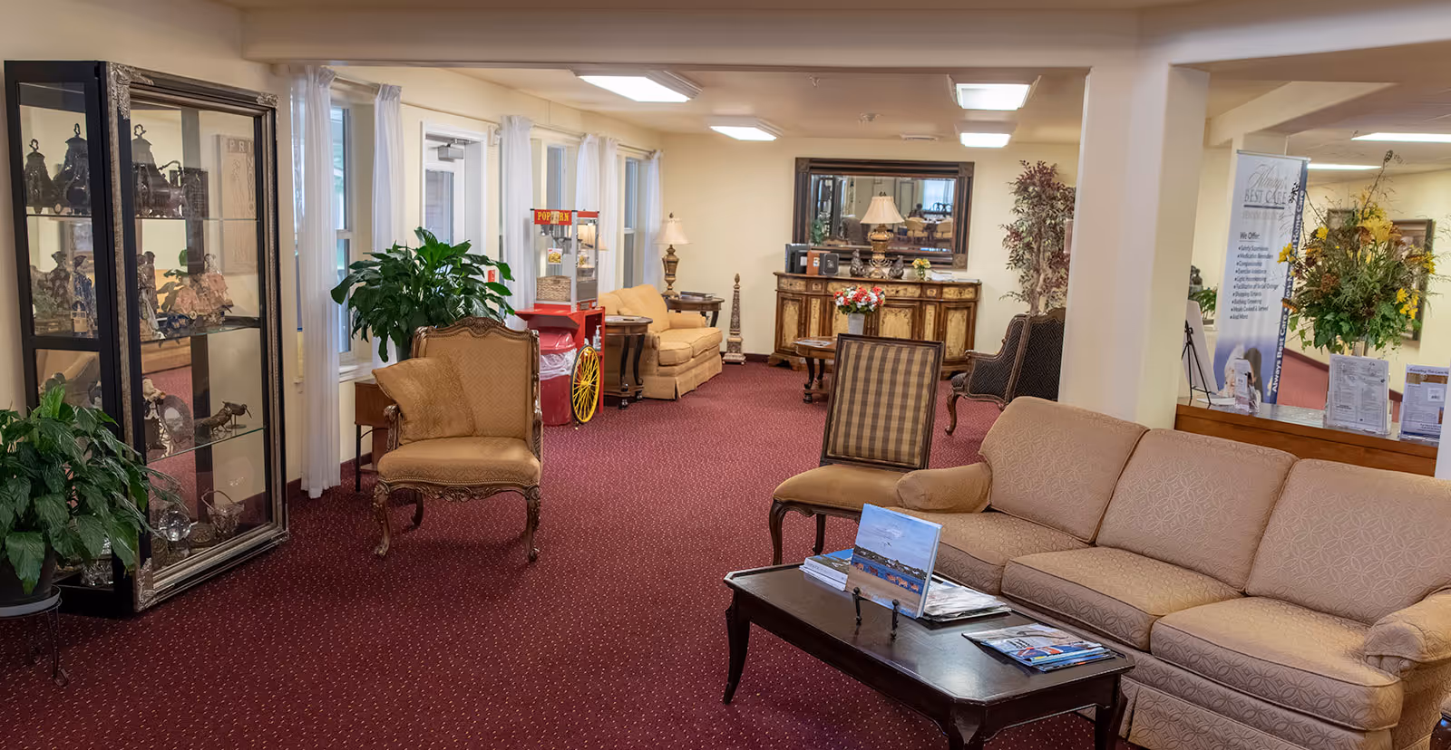 Carpeted lounge area with sofas, armchairs, a coffee table, display cabinet, plants, and decorative furnishings.