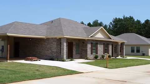 Single-story brick senior living building with a manicured lawn and driveway in daylight.
