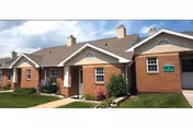Brick ranch-style senior living units with covered entrances, small lawns, and a paved walkway under a partly cloudy sky.