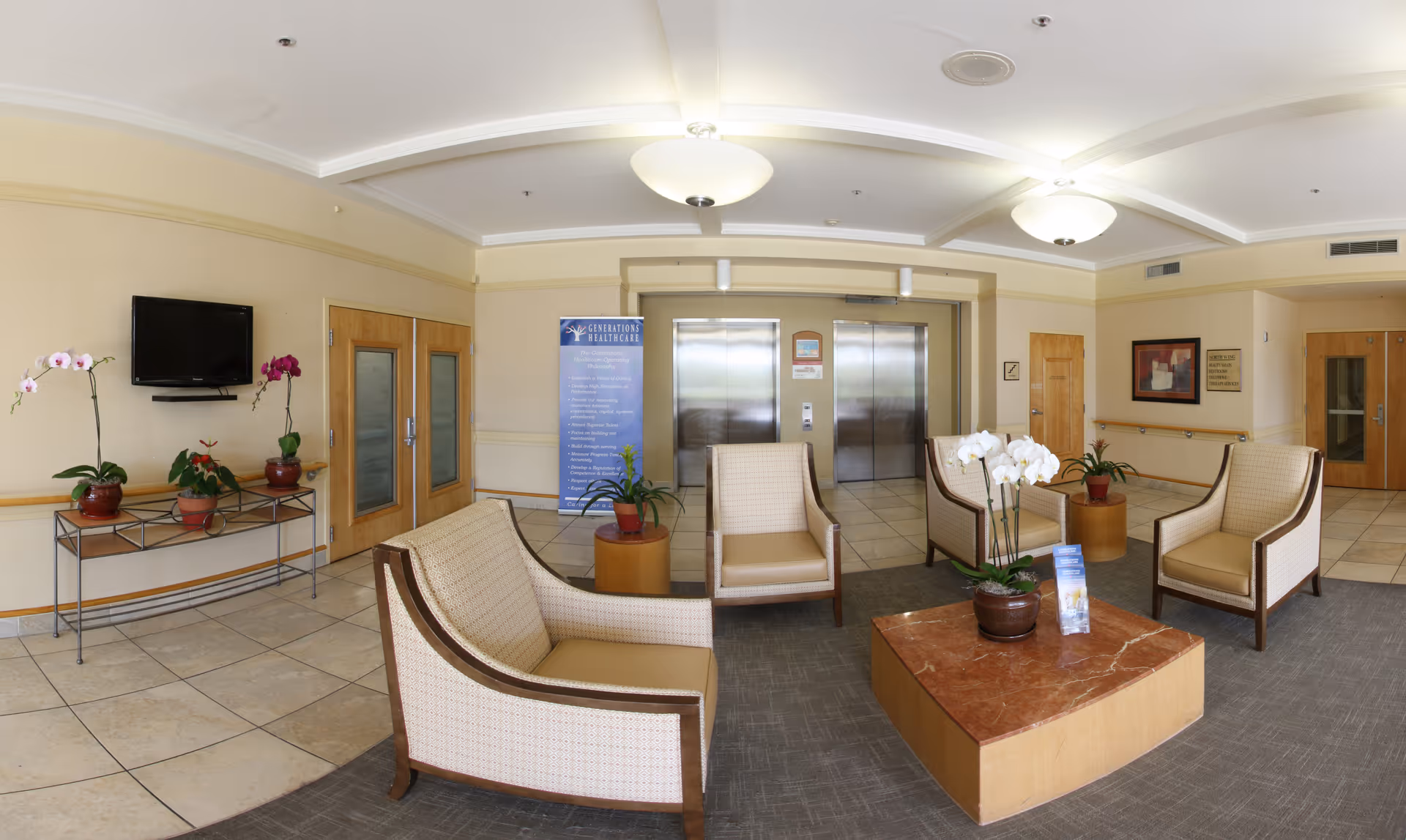 Lobby seating area with armchairs, a coffee table topped with an orchid, potted plants, and elevators in the background.