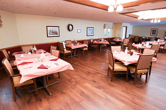 Dining room with multiple tables covered in pink tablecloths and chairs on wood flooring.