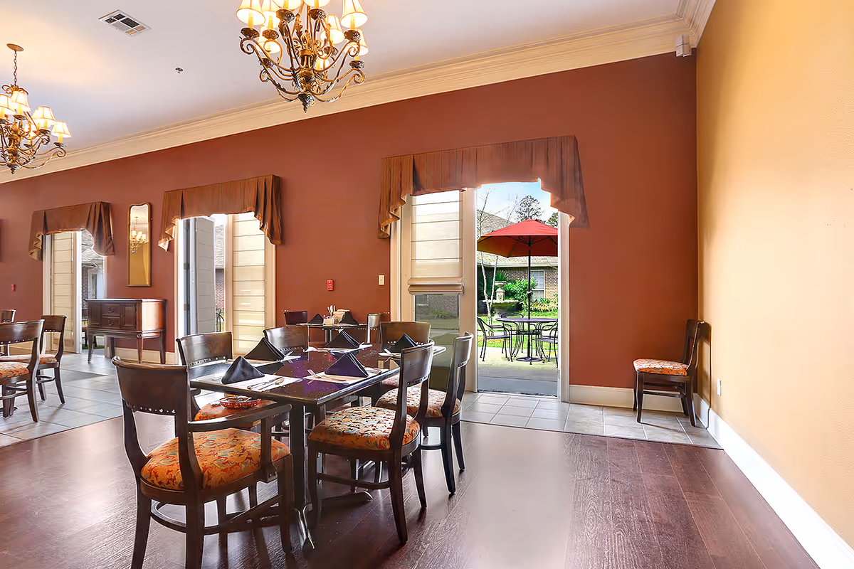 Dining room with tables and chairs, chandeliers, and an open door leading to an outdoor patio with a red umbrella.