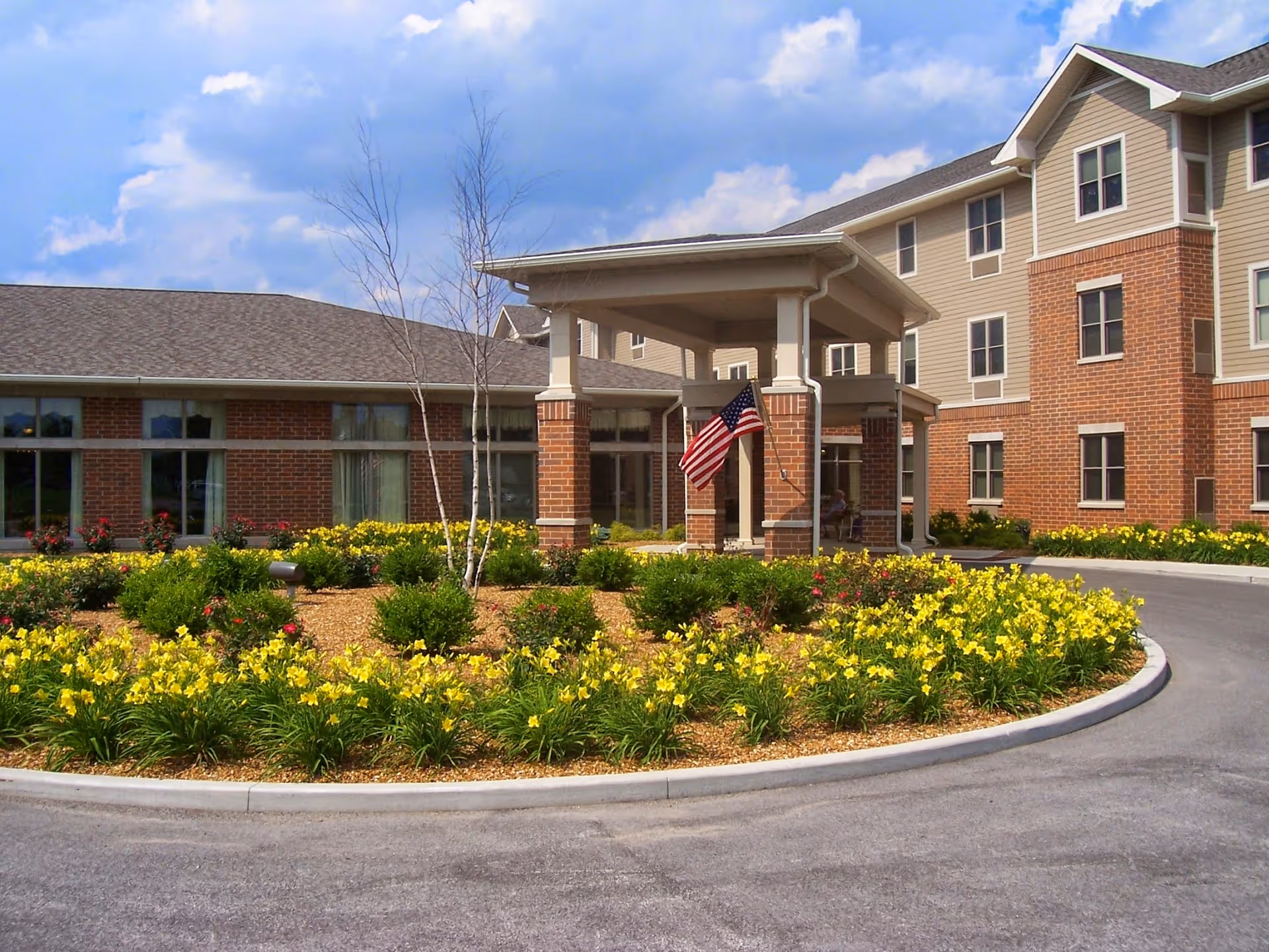Front entrance of Evergreen Senior Living facility with landscaped flower beds and flag.