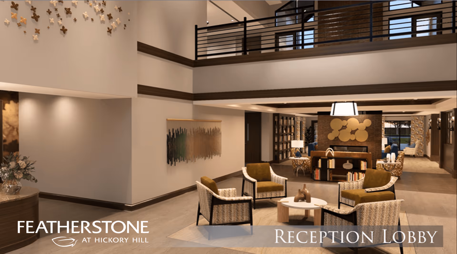 A spacious and modern reception lobby with a seating area consisting of four armchairs around a small round table. The lobby features a high ceiling with a balcony railing above, warm lighting, decorative wall art, and a bookshelf behind the seating area. The space has a welcoming and comfortable atmosphere.