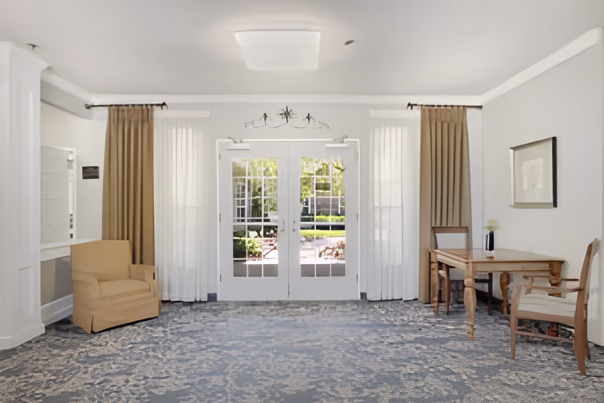 Bright interior seating area with chairs, a small table, and double glass doors leading outside.