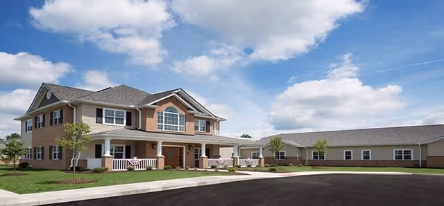 Exterior view of Kemper House Highland Heights, showing a two-story brick and siding building with a covered porch, several windows, and a paved driveway under a partly cloudy sky.