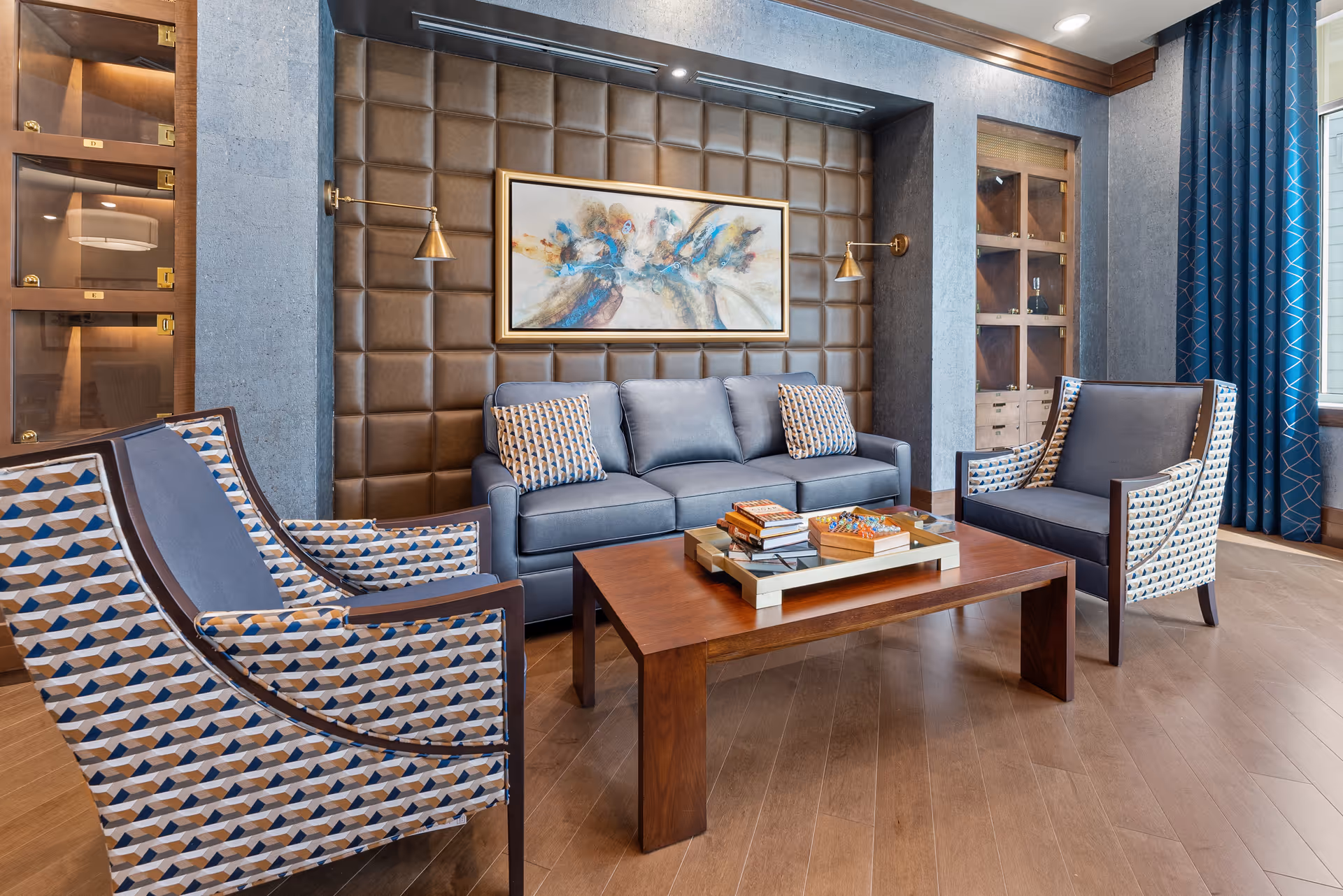 Stylish lounge with a blue sofa and patterned armchairs arranged around a wooden coffee table in front of a tufted leather accent wall and framed artwork.
