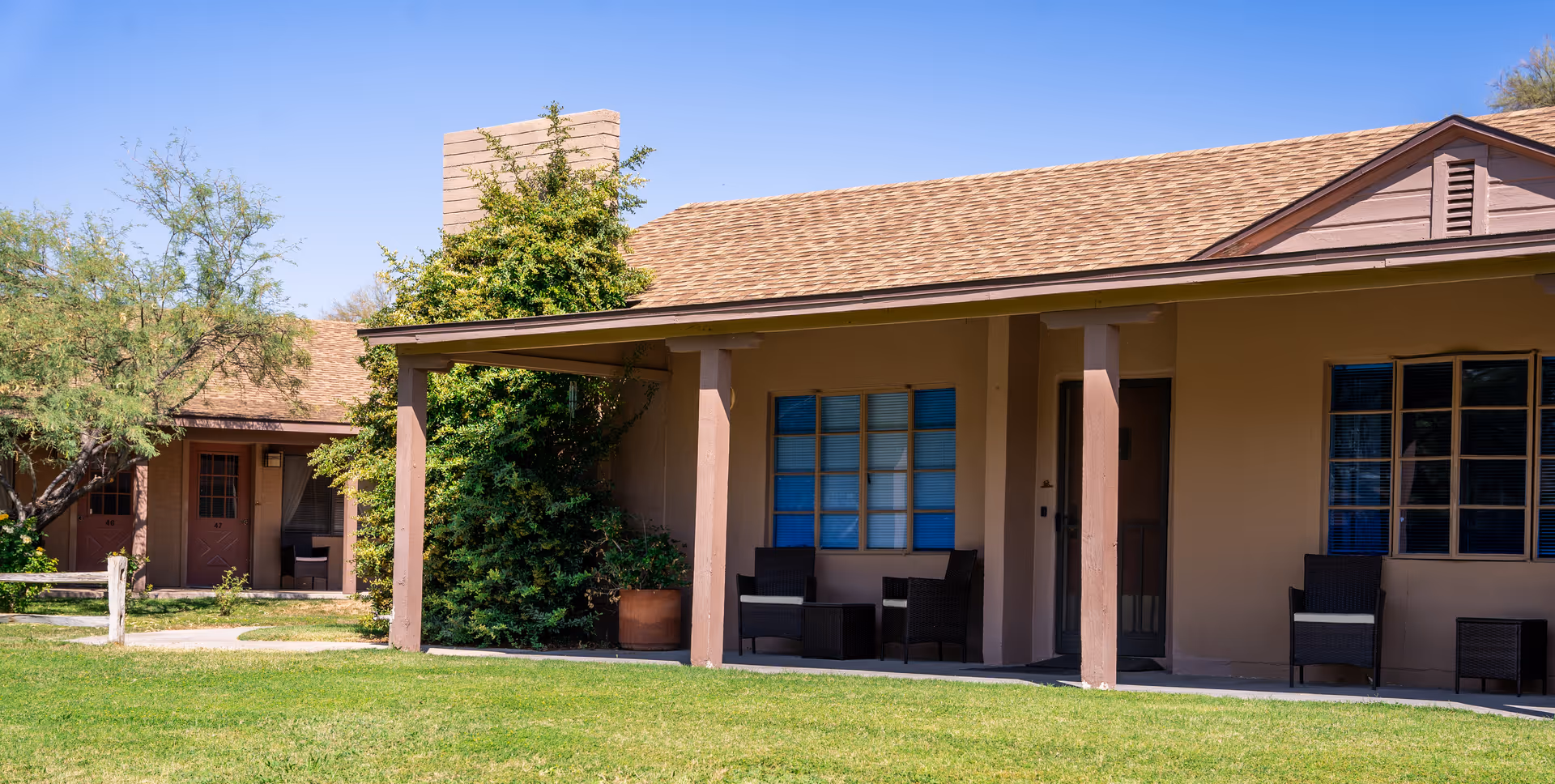 Single-story ranch-style senior living building with a covered porch, outdoor seating, windows, and a grassy lawn.