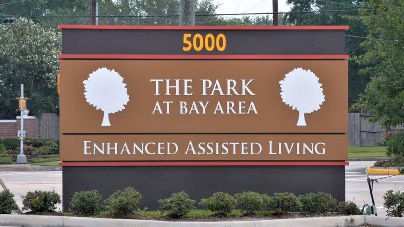 Roadside entrance sign reading '5000 The Park at Bay Area Enhanced Assisted Living' with two tree icons.