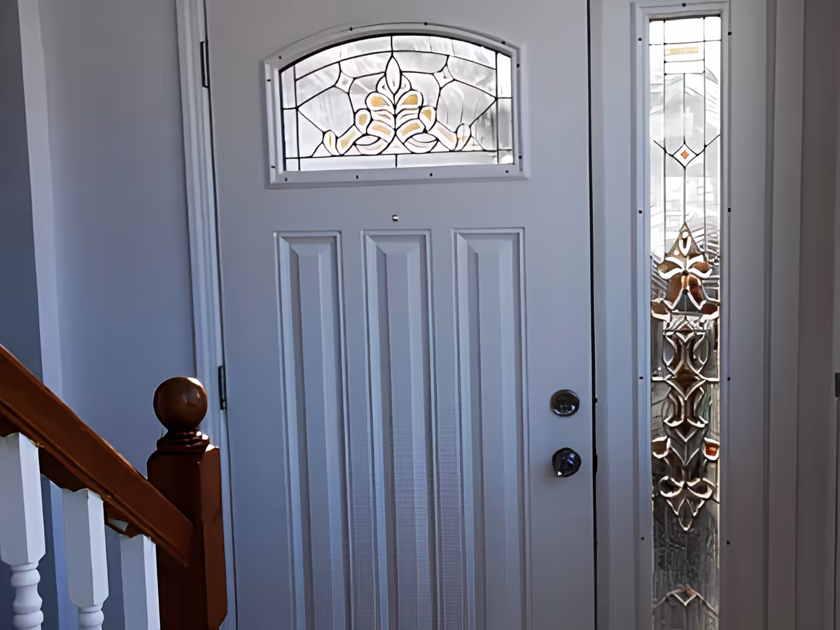 Interior view of a white front door with decorative stained-glass panels and a wooden staircase banister.