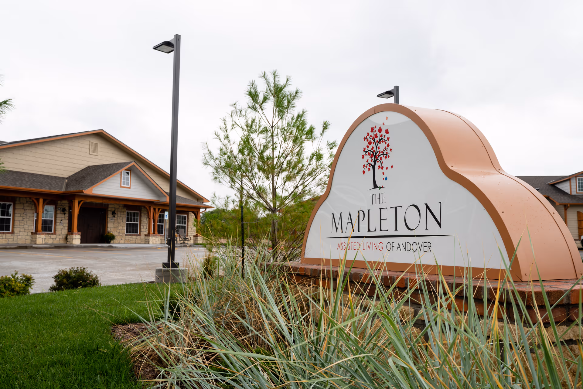 A large landscaped entrance sign reading "The Mapleton" in front of a single-story assisted living building.