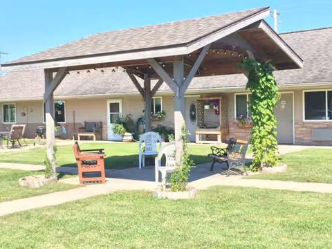 Outdoor communal seating area under a wooden pavilion in front of a building.