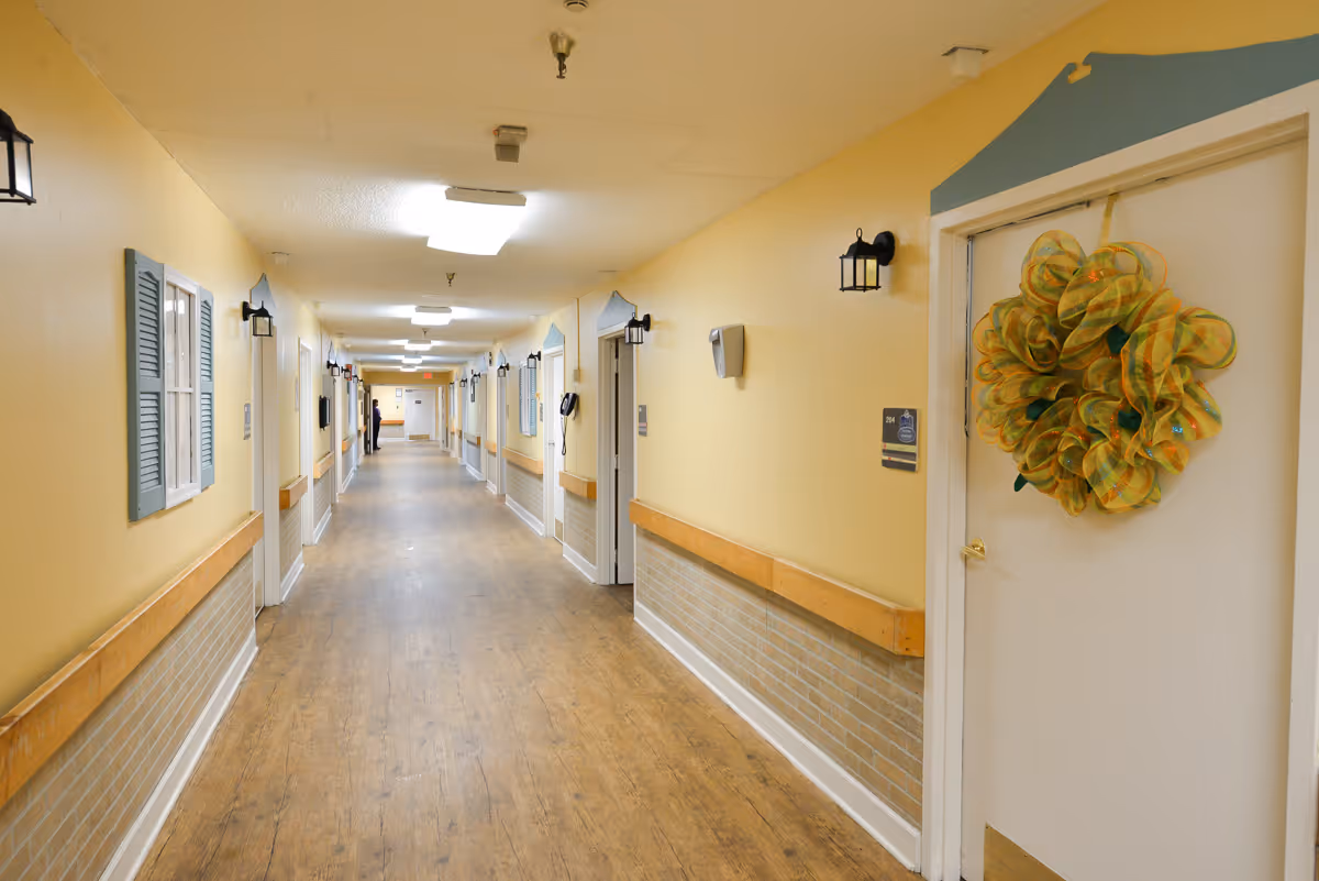 Long, well-lit hallway inside a senior living facility with yellow walls, wood floors and decorated doors.