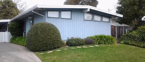 A single-story blue Shalom House facility with trimmed hedges, green lawn, and a driveway.