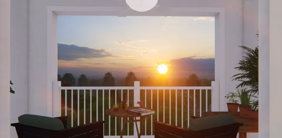 View of a balcony at sunset with two cushioned chairs, a small round table with a book and a bottle, and several potted plants on the side table and floor.