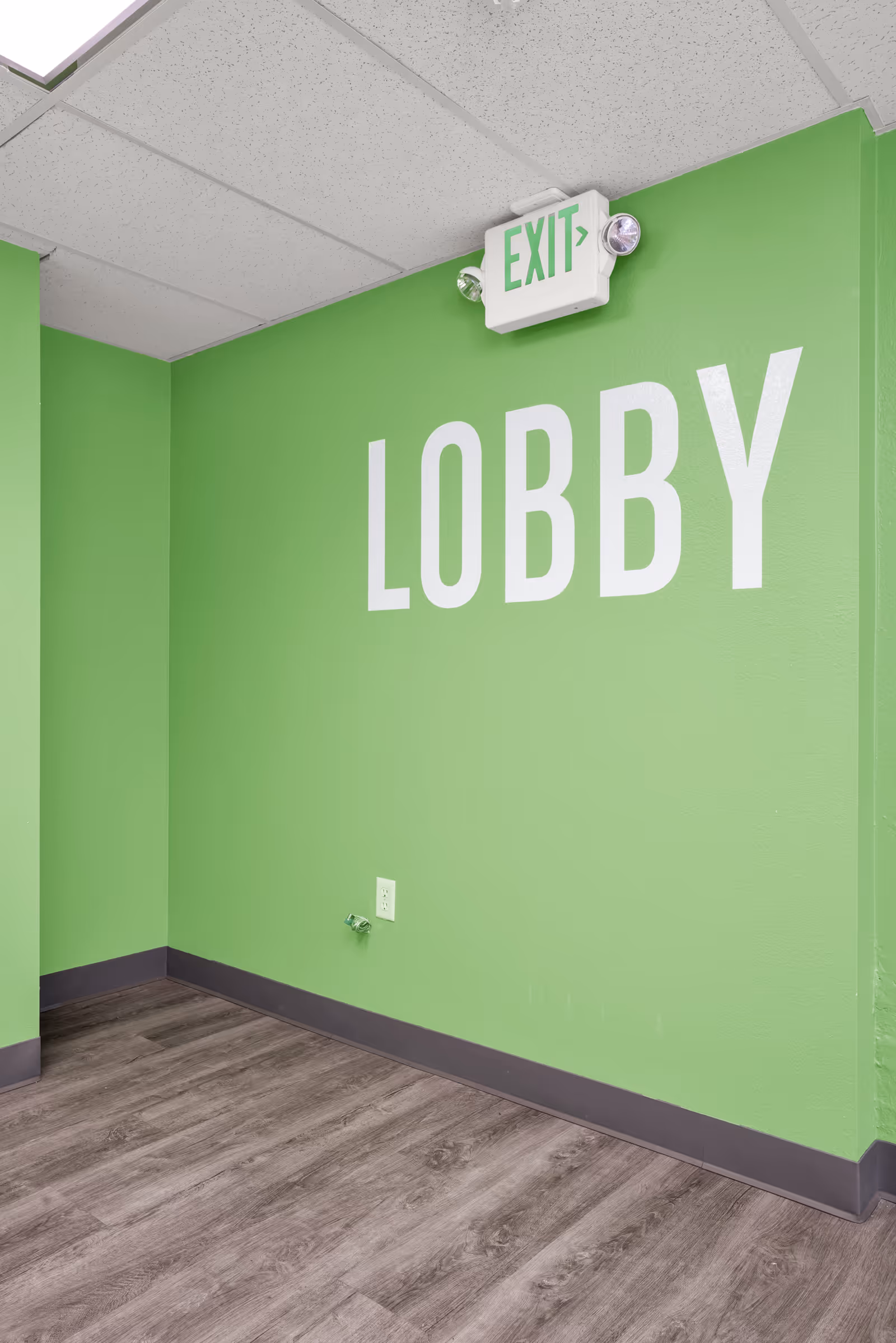 Green interior wall labeled 'LOBBY' with an illuminated EXIT sign above and wood-look flooring.