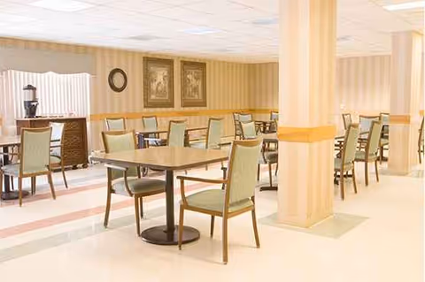 A spacious dining room with multiple tables and chairs in beige-toned decor.