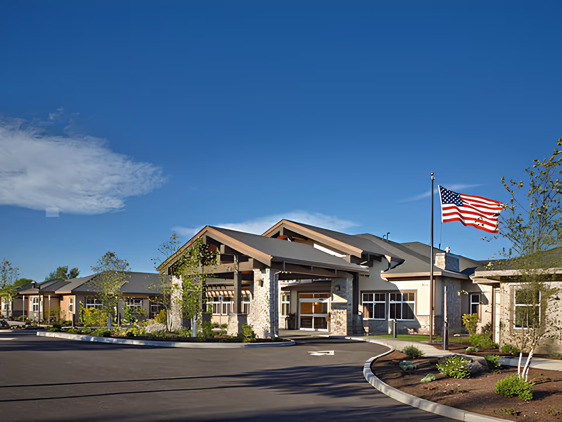 Front entrance of Bend Transitional Care building with an American flag flying on a pole under a clear blue sky.